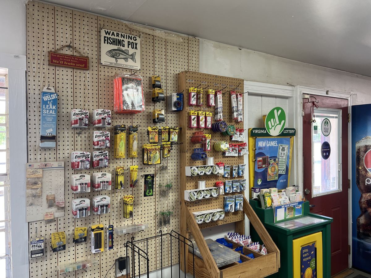 Pegboard wall of fishing tackle — Strike King and Eagle Claw lures, batteries, and the Virginia Lottery dispenser.